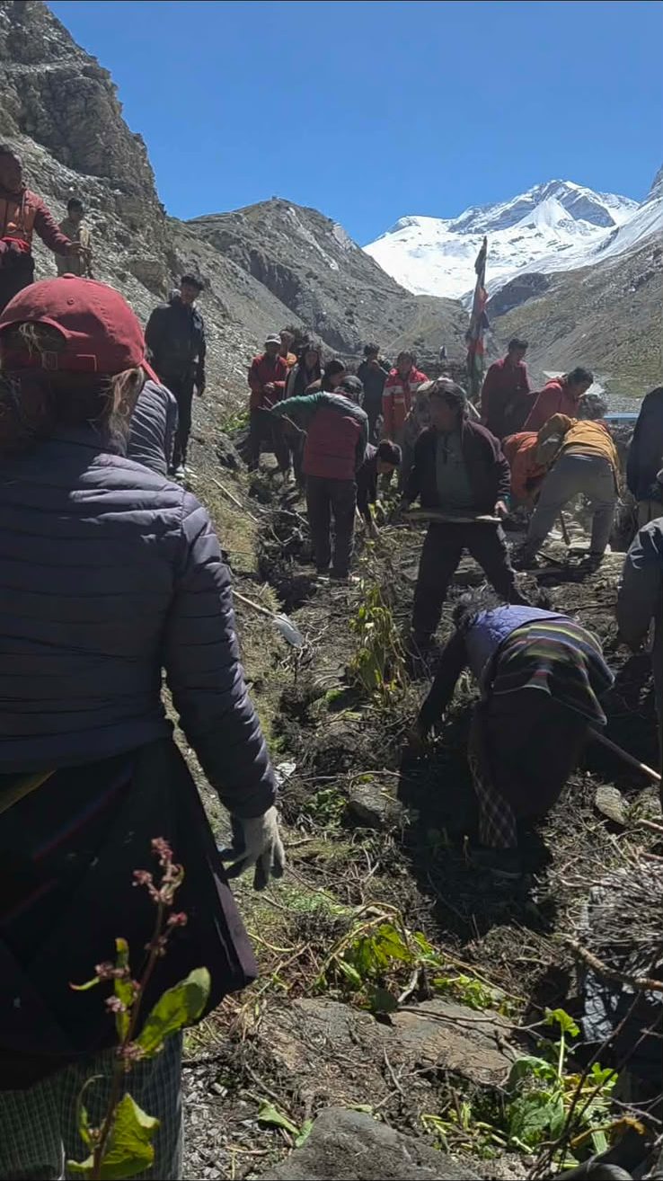 Villagers digging and clearing the slope below a snow peak